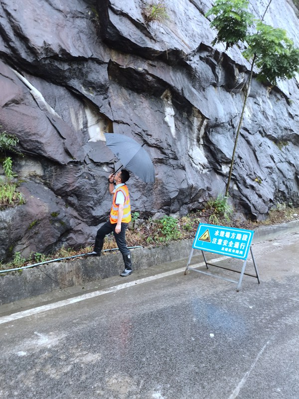 《看·守》。6月23日，208地質隊駐守隊員曹銳在北碚區天府鎮雨中巡查公路邊坡。