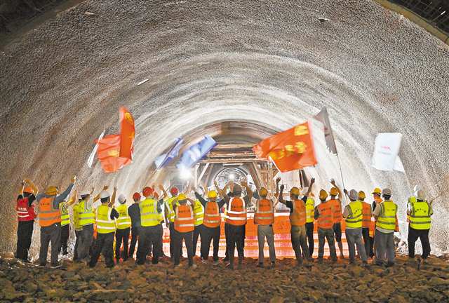 圖為建設者在塔平村隧道貫通點向對面掘進工友搖旗慶祝。